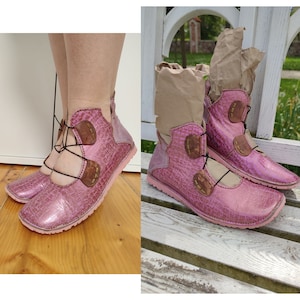May include: Pink leather ankle boots with brown leather accents and laces. The boots have a textured surface and a rounded toe.