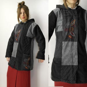 Puede incluir: Chaqueta negra con capucha con paneles de retazos grises y diseños florales bordados. La chaqueta presenta una textura acolchada y dos bolsillos delanteros. La modelo lleva una falda roja. La chaqueta está hecha de un material suave y cómodo.