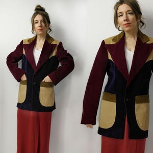 May include: A multi-colored corduroy blazer with a tailored fit. The jacket features panels of burgundy, navy, tan, and black. It has a notched collar, two front pockets, and a single-button closure. The sleeves are long and the blazer is worn over a white top.