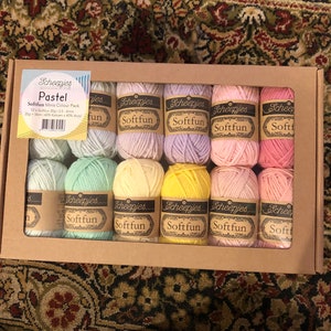 May include: A box set of Scheepjes Softfun Pastel Mini yarn packs. The box contains 12 mini skeins in various pastel colours, including pink, yellow, and blue. Each skein is labelled with the "Softfun" brand name.