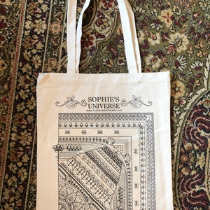 May include: A white canvas tote bag with black print. The print features a decorative design with the text "Sophie's Universe" and "www.lookatwhatimade.net". The bottom of the bag has the text "Scheepjes" and "Inspiration in every ball of yarn."