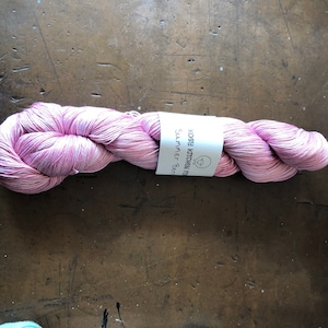 May include: A skein of pink yarn with a white label that reads "Kosy Kitchen Fibers Summer Berry".