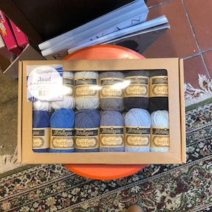 Könnte beinhalten: Eine Schachtel Scheepjes Softfun Garn in verschiedenen Blautönen. Die Schachtel enthält 12 Knäuel Garn, die jeweils mit dem Markennamen und der Farbe "Cloud" gekennzeichnet sind.