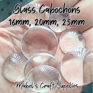May include: Clear glass cabochons in various sizes, including 16mm, 20mm, and 25mm, are displayed. The image features the text "Glass Cabochons" and "Mabel's Craft Supplies". The cabochons are round and transparent, suitable for crafting.