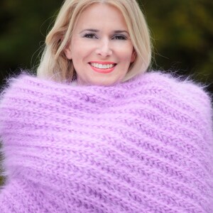 Peut inclure: Une femme aux cheveux blonds porte un pull en maille doux et moelleux de couleur lavande. Le pull est drap&eacute; autour de ses &eacute;paules et de son cou, cr&eacute;ant un look confortable et chaleureux.