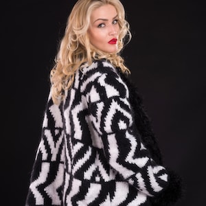 Op de afbeelding: Een zwart-wit gepatroneerde cardigan met een pluche rand. De cardigan is gemaakt van een zacht, pluche materiaal en heeft een ontspannen pasvorm.