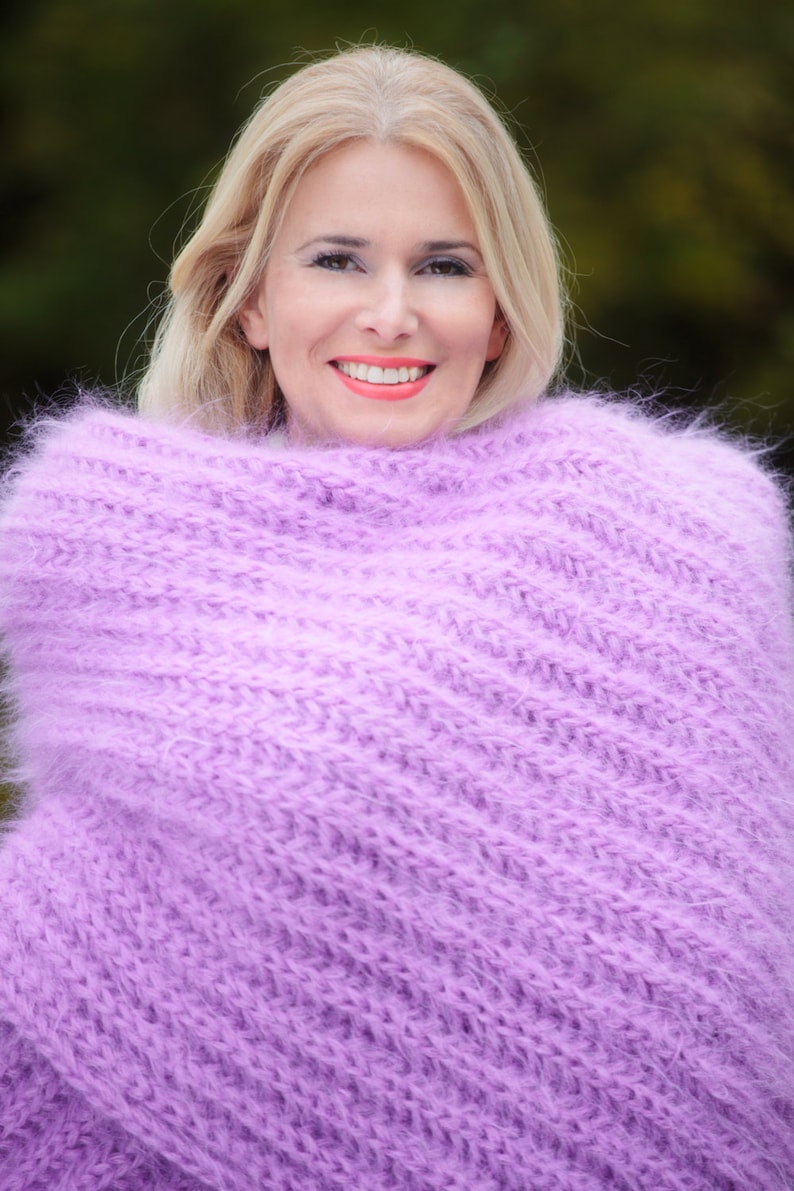 Peut inclure: Une femme aux cheveux blonds porte un pull en maille doux et moelleux de couleur lavande. Le pull est drap&eacute; autour de ses &eacute;paules et de son cou, cr&eacute;ant un look confortable et chaleureux.