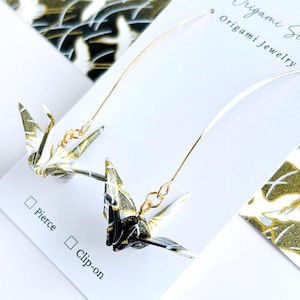 Op de afbeelding: Een paar origami-kraanvogel oorbellen met gouden accenten. De kranen zijn gemaakt van zwart en wit papier met gouden glitter. De oorbellen zijn verkrijgbaar in zowel steek- als clip-on stijlen.  Origami Jewelry.