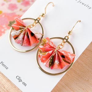 May include: Gold-coloured hoop earrings featuring origami fan pendants. The paper fans are in coral, white, and gold hues, with floral patterns. The earrings are labelled "Origami Jewelry" and are available as "Pierce" or "Clip-on".