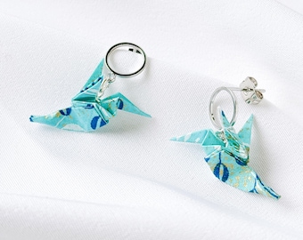 Può includere: Un paio di orecchini a cerchio color argento con pendenti a forma di gru origami. Le gru sono realizzate in carta azzurra con un motivo floreale blu scuro e dettagli dorati. Ogni orecchino è dotato di una chiusura a perno e farfallina.