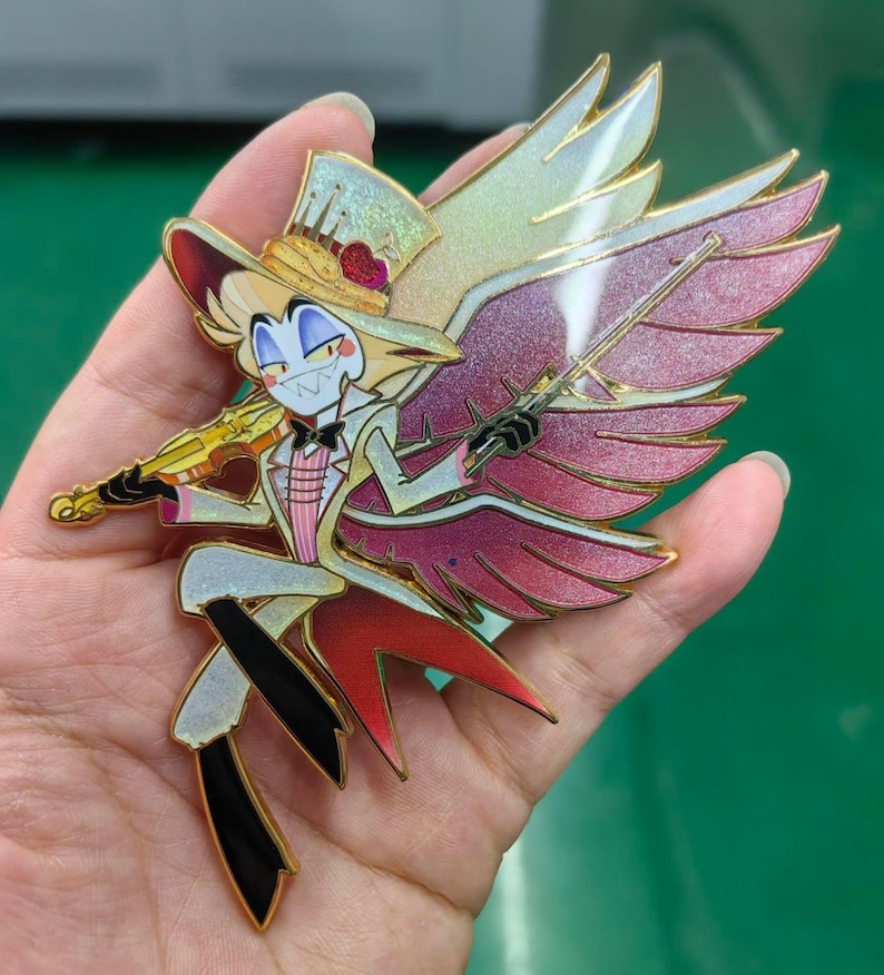 May include: A colorful enamel pin featuring a cartoon character with a top hat, bow tie, and wings, holding a violin. The pin has gold accents and a red, pink, and white color scheme. The character is smiling with sharp teeth.