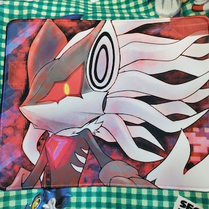 May include: A white and black mouse mat featuring a red-eyed, white and black wolf-like character with a red gem on its chest. The character has a white, flowing mane. The background is a red and black abstract design. The mouse mat has a white border and the text "SEGA THE HEDGHOG" in the top right corner.