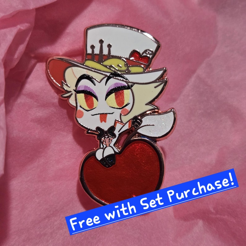 May include: A gold-colored enamel pin featuring a cartoon character with a white top hat, red eyes, and a red heart-shaped base. The pin has a glittery white wing and the text "Free with Set Purchase!" on a blue banner.