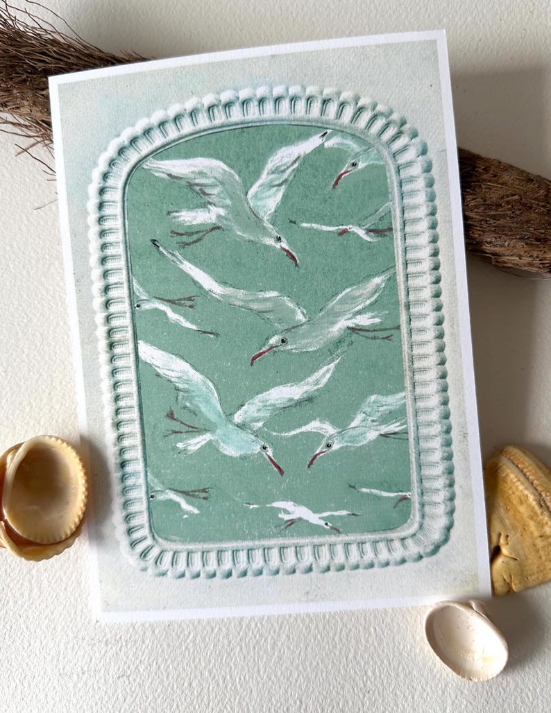 Puede incluir: Una impresi&oacute;n que representa una bandada de gaviotas blancas con picos rojos, sobre un fondo verde azulado dentro de un marco decorativo. La obra de arte est&aacute; en una tarjeta blanca, con conchas marinas y acentos de madera flotante.