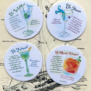 May include: Four round white coasters featuring watercolor illustrations of cocktails titled The Wellfleet, The Ptown, The Falmouth, and The Martha's Vineyard. Each coaster includes a unique recipe list and descriptive text in a cursive script font.