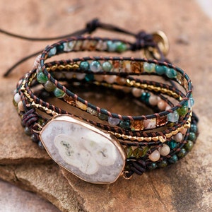 May include: Multi-strand bracelet with brown leather cord, gold beads, and various green, blue, and white stones. A large white agate stone is the centerpiece of the bracelet.