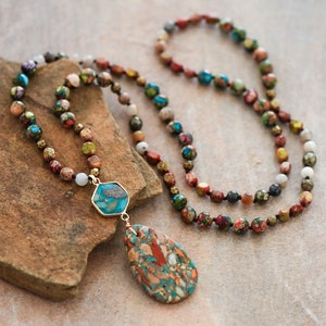 May include: A multi-colored beaded necklace with a teardrop-shaped pendant made of a colorful stone. The necklace is made of various sizes and colors of beads, including red, green, blue, and brown.