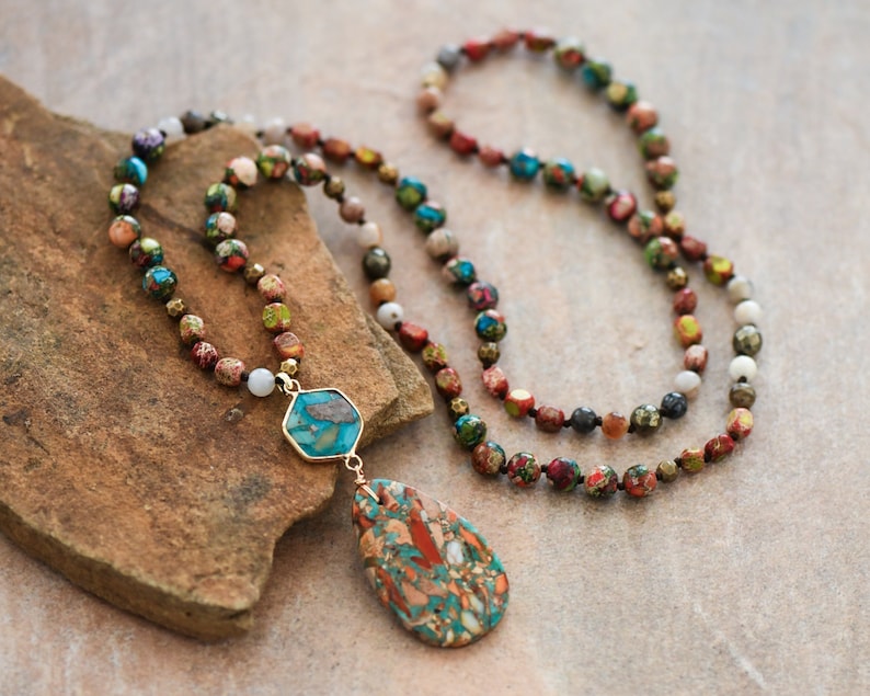 May include: A multi-colored beaded necklace with a teardrop-shaped pendant made of a colorful stone. The necklace is made of various sizes and colors of beads, including red, green, blue, and brown.