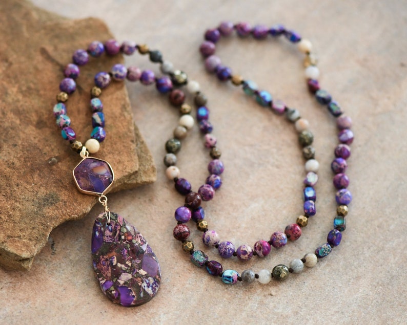 Peut inclure: Un long collier de perles violettes et dor&eacute;es avec un grand pendentif en pierre violette et dor&eacute;e.