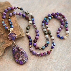 Peut inclure: Un long collier de perles violettes, bleues et dor&eacute;es avec un grand pendentif violet et dor&eacute;. Le collier est fait de pierres naturelles et est parfait pour &ecirc;tre superpos&eacute;.