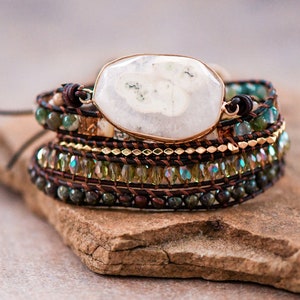 May include: A multi-layered bracelet with a large white agate gemstone, brown leather cord, and green and gold beads.
