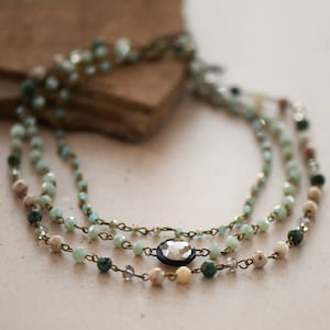 May include: A layered necklace with green, white, and brown beads and a clear crystal pendant.