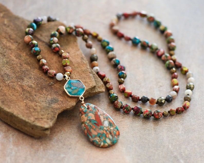 May include: A multi-strand necklace made of colorful, patterned beads with a teardrop-shaped pendant. The pendant is made of a stone with a mix of red, green, and brown colors.