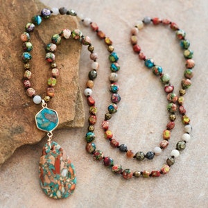 May include: A long multi-strand necklace with a teardrop-shaped pendant. The necklace is made of small, colorful beads and features a gold-toned metal accent. The pendant is made of a turquoise and brown stone.