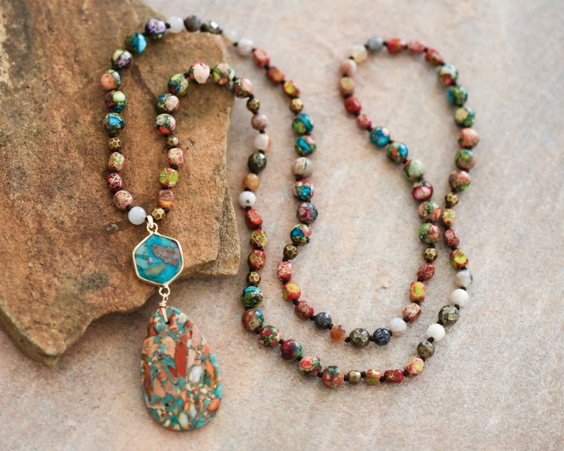 May include: A long multi-strand necklace with a teardrop-shaped pendant. The necklace is made of small, colorful beads and features a gold-toned metal accent. The pendant is made of a turquoise and brown stone.