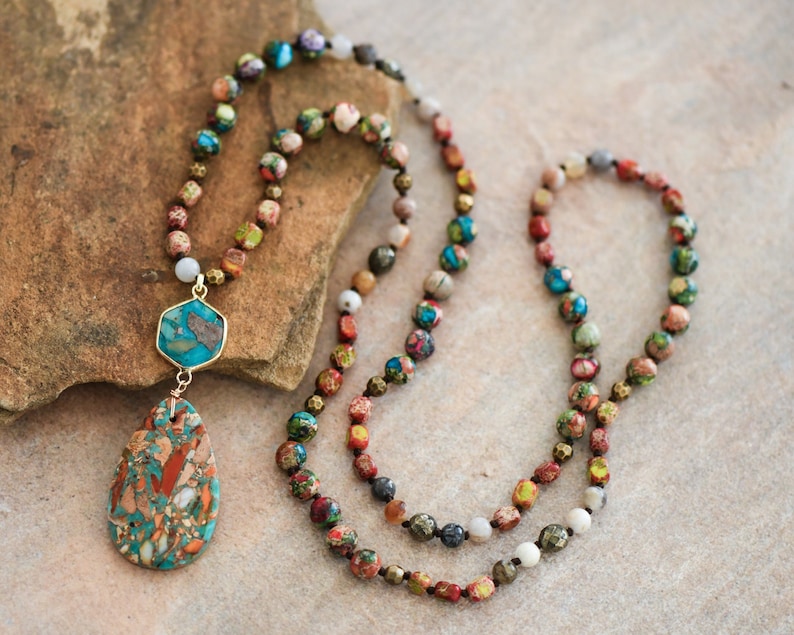 May include: A multi-strand necklace made of colorful, patterned beads with a teardrop-shaped pendant. The pendant is made of a light blue, brown, and white stone.