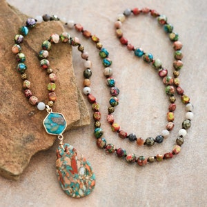 May include: A long multi-colored beaded necklace with a teardrop-shaped pendant. The pendant is made of a mix of turquoise, brown, and white stones. The necklace is made of various stones, including turquoise, brown, white, and gold.