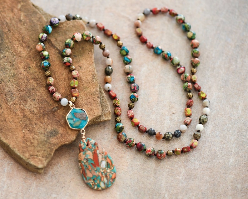 May include: A long multi-colored beaded necklace with a teardrop-shaped pendant. The pendant is made of a mix of turquoise, brown, and white stones. The necklace is made of various stones, including turquoise, brown, white, and gold.