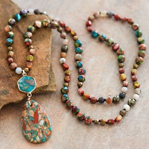 May include: A multi-strand necklace with a teardrop-shaped pendant. The necklace is made of small, colorful beads and features a large, turquoise-colored stone in the pendant.