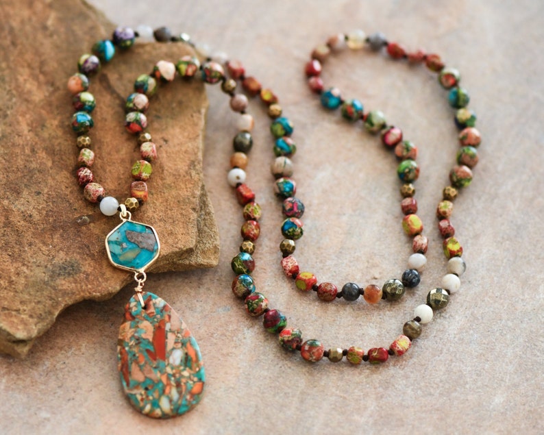 May include: A multi-strand necklace with a teardrop-shaped pendant. The necklace is made of small, colorful beads and features a large, turquoise-colored stone in the pendant.
