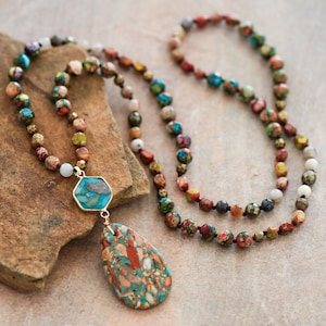 May include: A long necklace made of colorful beads with a turquoise and brown stone pendant. The necklace is on a brown textured surface.