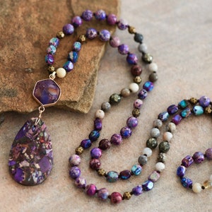 Peut inclure: Un long collier de perles violettes, bleues et brunes avec un grand pendentif en pierre violette et brune.