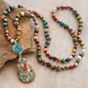 May include: A long multi-colored beaded necklace with a large turquoise and brown stone pendant. The necklace is made of various sizes and shapes of beads, including round, square, and hexagonal beads.