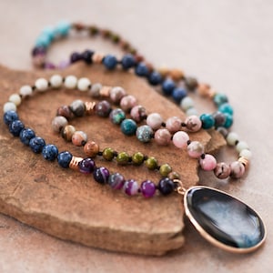 May include: A multi-colored gemstone necklace with a large black gemstone pendant. The necklace is made of various stones, including blue, green, pink, and brown.
