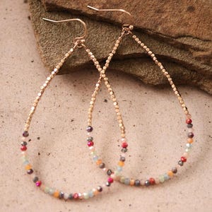 May include: A pair of teardrop-shaped earrings. The earrings have a gold-colored metal frame and are adorned with small, colorful beads in shades of red, orange, pink, and blue. The earrings are displayed against a neutral background.