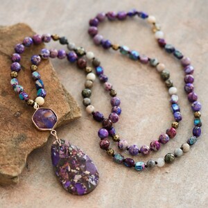 Peut inclure: Un long collier de perles violettes et dor&eacute;es avec un pendentif en pierre pr&eacute;cieuse violette. Le collier est compos&eacute; de perles de diff&eacute;rentes tailles et formes, dont certaines sont iris&eacute;es.
