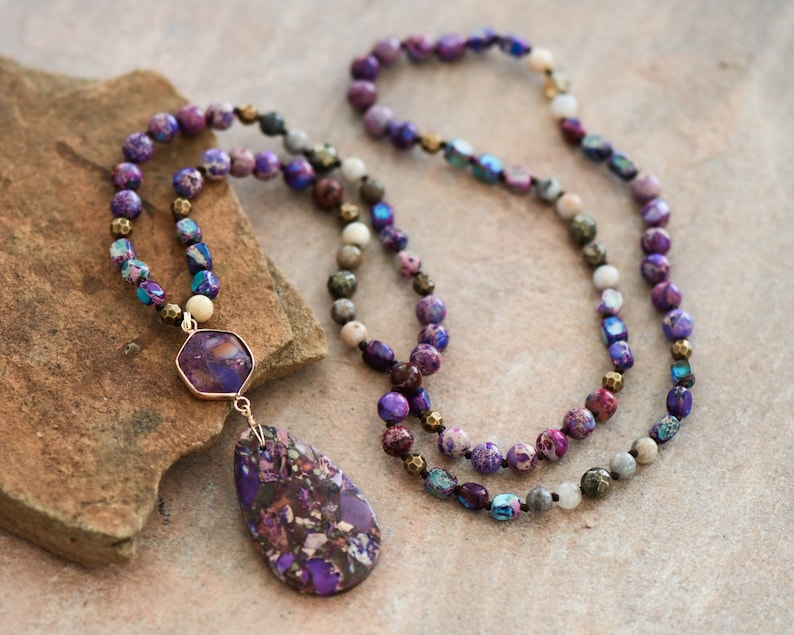 Peut inclure: Un long collier de perles violettes et dor&eacute;es avec un pendentif en pierre pr&eacute;cieuse violette. Le collier est compos&eacute; de perles de diff&eacute;rentes tailles et formes, dont certaines sont iris&eacute;es.