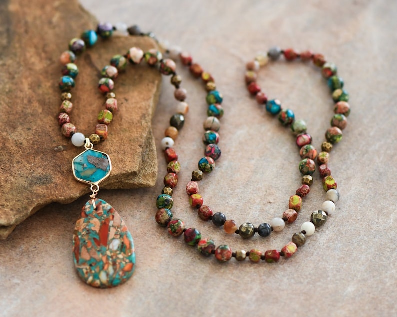 May include: A multi-strand necklace with a teardrop-shaped pendant. The necklace is made of various colored beads, including red, green, blue, and brown. The pendant is made of a blue and brown stone.
