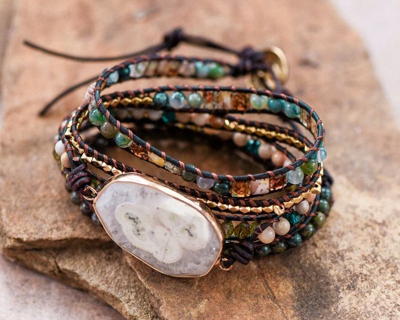 May include: Multi-strand bracelet with brown leather cord, gold beads, and various green, blue, and white stones. A large white agate stone is the centerpiece of the bracelet.