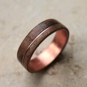 May include: A wooden ring with a copper band. The wood is a dark brown color and has a natural grain pattern. The copper band is polished and shiny.