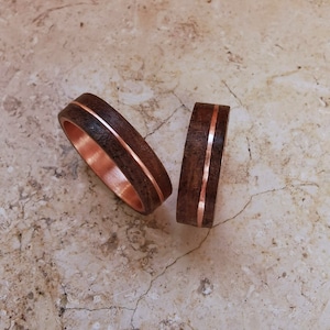 Könnte beinhalten: Zwei Holzringe mit einer Kupfereinlage. Die Ringe sind dunkelbraun und haben eine glatte Oberfläche.