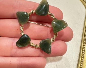 Pode incluir: Um broche dourado com um design de fio torcido e cinco pedras verdes. As pedras têm uma forma irregular e uma cor verde manchada.