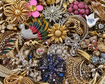 Könnte beinhalten: Eine Sammlung verschiedener Vintage-Broschen und Anstecknadeln mit diversen Motiven, darunter ein bunter Vogel, eine Sonnenblume, florale Muster und geometrische Formen. Die Stücke bestehen aus goldfarbenem Metall, Strass und Emaille-Akzenten.