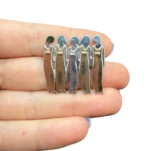 May include: A silver brooch depicting six figures in long dresses. Each figure has a heart-shaped detail on the chest. The figures are arranged together, suggesting a bond. The brooch has a polished finish, reflecting light and adding a touch of elegance.