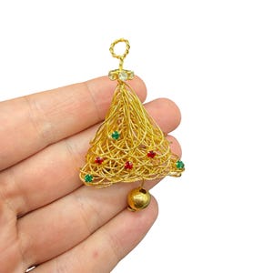 May include: A gold-colored wire Christmas tree ornament. The tree is adorned with red and green jewels and a small gold bell at the bottom. The top has a loop for hanging and a cluster of clear jewels.
