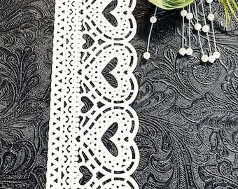 May include: White lace trim with a scalloped edge and a repeating heart design. The lace is on a black textured background.